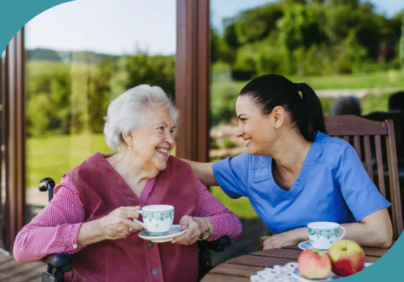 Elderly woman and caregiver enjoying tea outdoors.